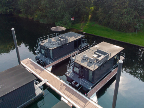 Vista aérea de dos modernas casas flotantes atracadas en Marina Mookerplas, rodeadas de naturaleza.