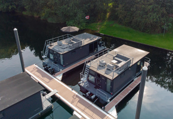 Vista aerea di due moderni houseboat ormeggiati a Marina Mookerplas, circondati da verde e acqua.