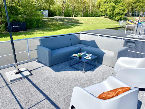 Gemütliche Sitzecke auf dem Hausboot Marina Mookerplas mit Sofa, Stühlen und Blick ins Grüne.