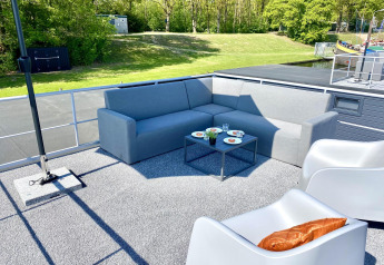 Area lounge esterna su Houseboat Marina Mookerplas con divano, poltrone e tavolo vista sul verde.