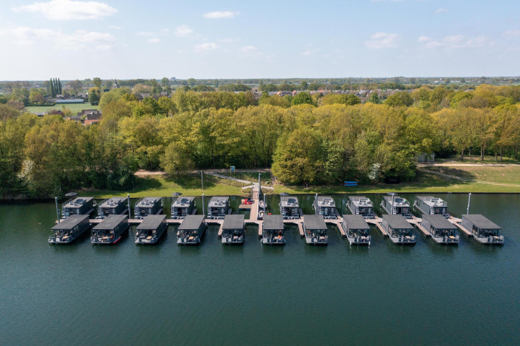 Vista aérea de casas flotantes en Houseboat Marina Mookerplas, Países Bajos, junto a la costa arbolada.
