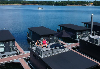 Twee mensen ontspannen op het dak van een woonboot bij Marina Mookerplas, omgeven door water en natuur.