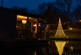 Hausboot an der Marina Mookerplas in den Niederlanden bei Nacht, beleuchteter Weihnachtsbaum draußen.