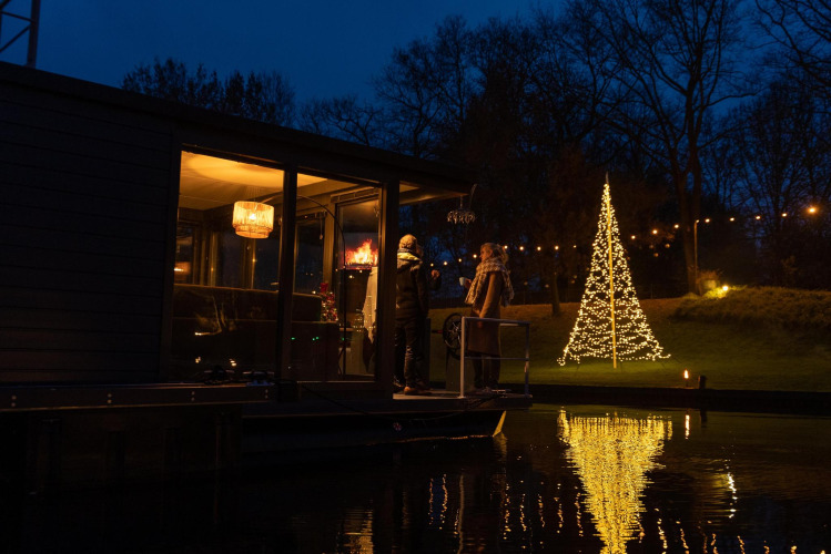 Casa flotante en Marina Mookerplas, Países Bajos, de noche, con dos personas y un árbol de Navidad iluminado.