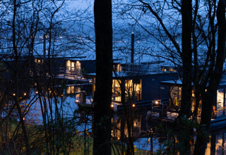 Aftenudsigt over oplyste husbåde ved Houseboat Marina Mookerplas omgivet af træer i Holland.