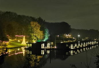 Foto notturna di una houseboat alla Marina Mookerplas nei Paesi Bassi con alberi illuminati e riflessi.