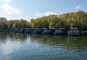 Una fila di moderne houseboat ormeggiate alla Marina Mookerplas nei Paesi Bassi con alberi sullo sfondo.