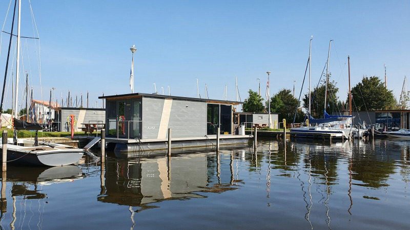 Casa flotante en Marina Heeg, Países Bajos, rodeada de veleros y agua tranquila en un día soleado.