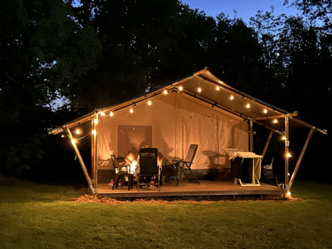 Safaritent met terras en lichtjes bij Camping Emmen in Nederland, ’s avonds genomen met mensen buiten.