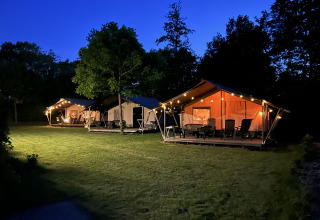 Tiendas safari iluminadas y terraza en Camping Emmen, Países Bajos, fotografiadas al anochecer.