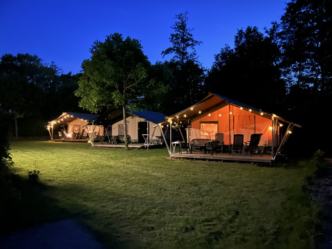 Tiendas safari iluminadas y terraza en Camping Emmen, Países Bajos, fotografiadas al anochecer.