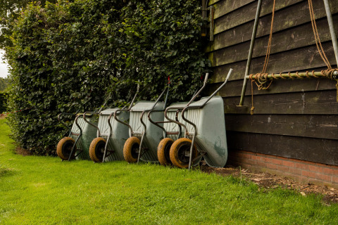 Four wheelbarrows lined up beside a wooden building and hedge in Feather Down Landgoed Volenbeek, Gelderland, Netherlands.