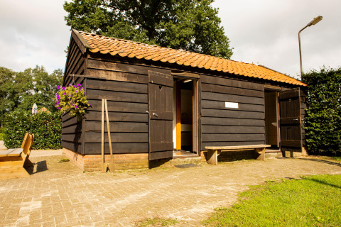 Piccola casetta nera in legno con tetto in tegole al parco vacanze Feather Down Landgoed Volenbeek in Gelderland.