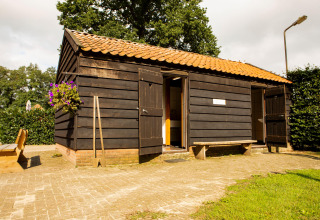 Piccola casetta nera in legno con tetto in tegole al parco vacanze Feather Down Landgoed Volenbeek in Gelderland.