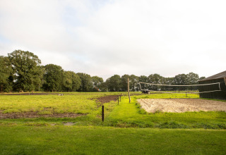 Un champ vert avec un filet de volley et terrain de sable près d'une grange à Landgoed Volenbeek, Gelderland.
