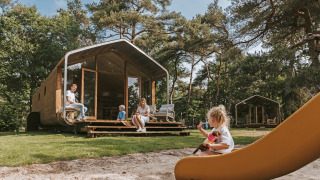 Gezin ontspant bij Wikkelhouse XL lodge in het groen, kinderen spelen buiten op de speeltuin.
