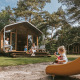 Familia disfruta del día en la Wikkelhouse XL lodge, con niños jugando en el tobogán al aire libre.