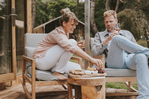 Pareja disfruta de vino y aperitivos en la terraza de Wikkelhouse XL lodge en Beerze Bulten, Países Bajos.