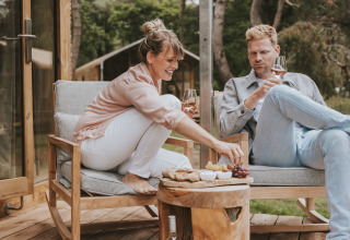 Pareja disfruta de vino y aperitivos en la terraza de Wikkelhouse XL lodge en Beerze Bulten, Países Bajos.