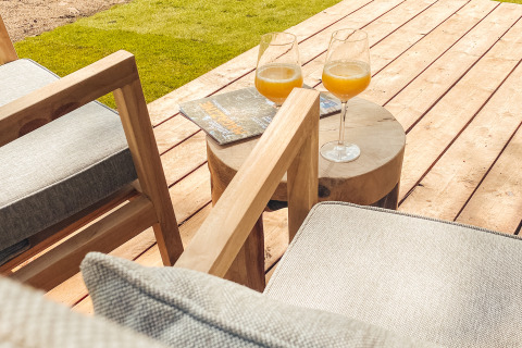Terrasse extérieure de lodge avec deux verres de jus d’orange, fauteuils en bois et table basse avec magazines.