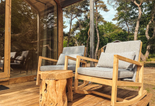 Terraza exterior de Wikkelhouse XL en Beerze Bulten, Países Bajos, con dos mecedoras y mesa de madera.