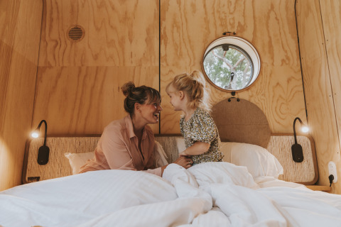 Moeder en dochter genieten samen in bed in de Wikkelhouse XL lodge bij Beerze Bulten, Nederland.