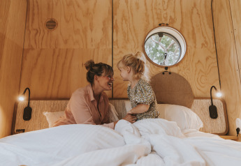 Madre e figlia sorridono insieme a letto nel lodge Wikkelhouse XL presso Beerze Bulten, Paesi Bassi.