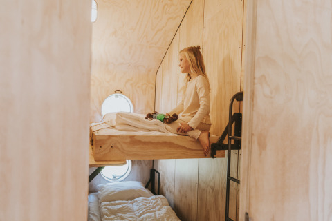 Niña sentada en la litera superior con paneles de madera en Wikkelhouse XL lodge en Beerze Bulten, Países Bajos.
