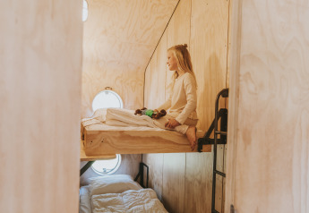 Niña sentada en la litera superior con paneles de madera en Wikkelhouse XL lodge en Beerze Bulten, Países Bajos.