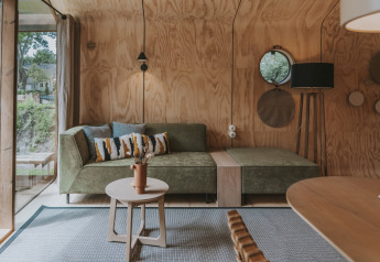 Moderne stue i Wikkelhouse XL ved Beerze Bulten, Holland, med grøn sofa, trævægge og klart lysindfald.