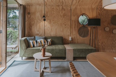 Sala moderna en Wikkelhouse XL en Beerze Bulten, Países Bajos, con sofá verde y paredes de madera clara iluminadas.