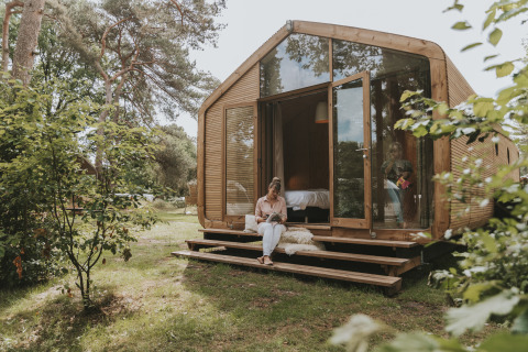 Vrouw leest een boek op de trap van een moderne Wikkelhouse XL lodge te midden van groen bij Beerze Bulten, Nederland.