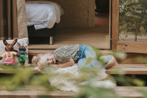 Un bambino sorridente sdraiato su una coperta davanti a Wikkelhouse XL lodge a Beerze Bulten, Paesi Bassi.