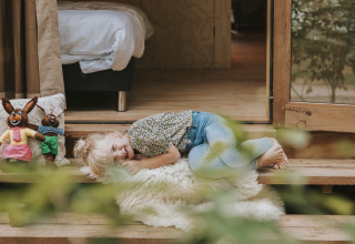 Un enfant souriant allongé sur une couverture devant Wikkelhouse XL lodge à Beerze Bulten, Pays-Bas.