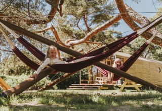 Due bambini giocano sulle amache sotto gli alberi davanti alla Wikkelhouse XL presso Beerze Bulten, Paesi Bassi.