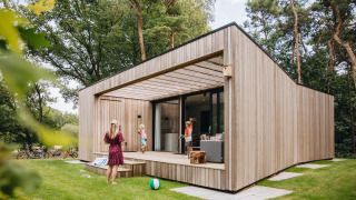Moderne Hill Lodge met houten bekleding, terras en mensen die buiten in het bos genieten.