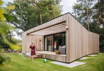 Moderne Hill Lodge met houten bekleding, terras en mensen die buiten in het bos genieten.