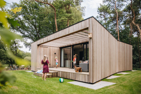 Lodge Hill moderno con fachada de madera, terraza y personas disfrutando actividades al aire libre.