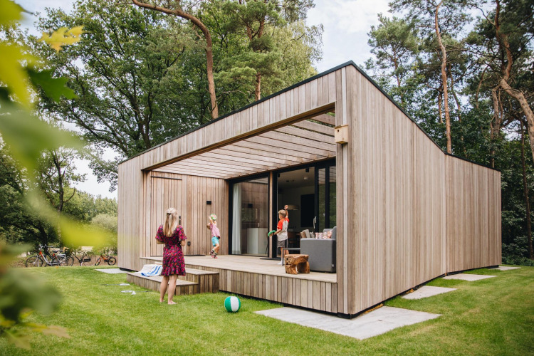 Lodge Hill moderno con fachada de madera, terraza y personas disfrutando actividades al aire libre.