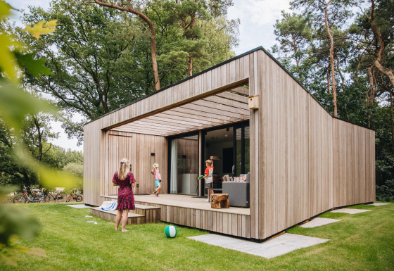 Lodge Hill moderno con fachada de madera, terraza y personas disfrutando actividades al aire libre.