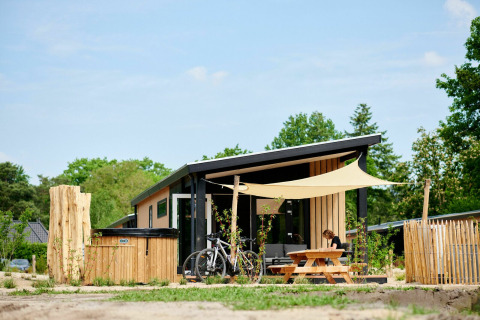 Tiny house Sand Lodge Jacuzzi con bicicletas y mesa de picnic en Holiday Park De IJsvogel, Países Bajos, rodeado de naturaleza.