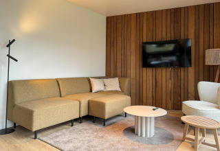 Salón moderno en Hill Lodge, Beerze Bulten, Países Bajos con sofá, pared de madera y televisor.