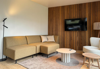 Salón moderno en Hill Lodge, Beerze Bulten, Países Bajos con sofá, pared de madera y televisor.