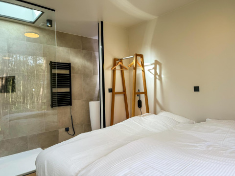 Dormitorio moderno en Hill Lodge, Beerze Bulten, Países Bajos, con cama doble y ducha de vidrio visible.