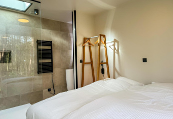 Dormitorio moderno en Hill Lodge, Beerze Bulten, Países Bajos, con cama doble y ducha de vidrio visible.