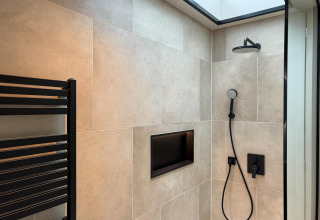Modern shower with black fixtures, wall-mounted niche, and skylight at Hill Lodge in Beerze Bulten, Netherlands.