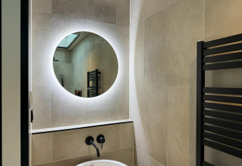 Moderne badkamer met ronde, verlichte spiegel bij de wastafel in Hill Lodge bij Beerze Bulten, Nederland.