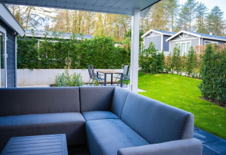 Zona de estar al aire libre con sofá gris y jardín en Heuvelrug Cottage, De Thijmse Berg, Países Bajos.