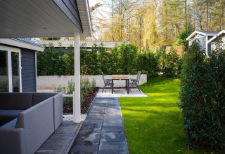 Patio moderno con zona de asientos y césped en Heuvelrug Cottage, De Thijmse Berg, Países Bajos, rodeado de árboles.