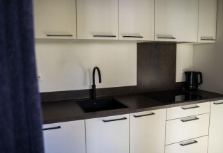 Cocina moderna en Heuvelrug Cottage con armarios blancos, fregadero negro, hervidor y vitrocerámica.
